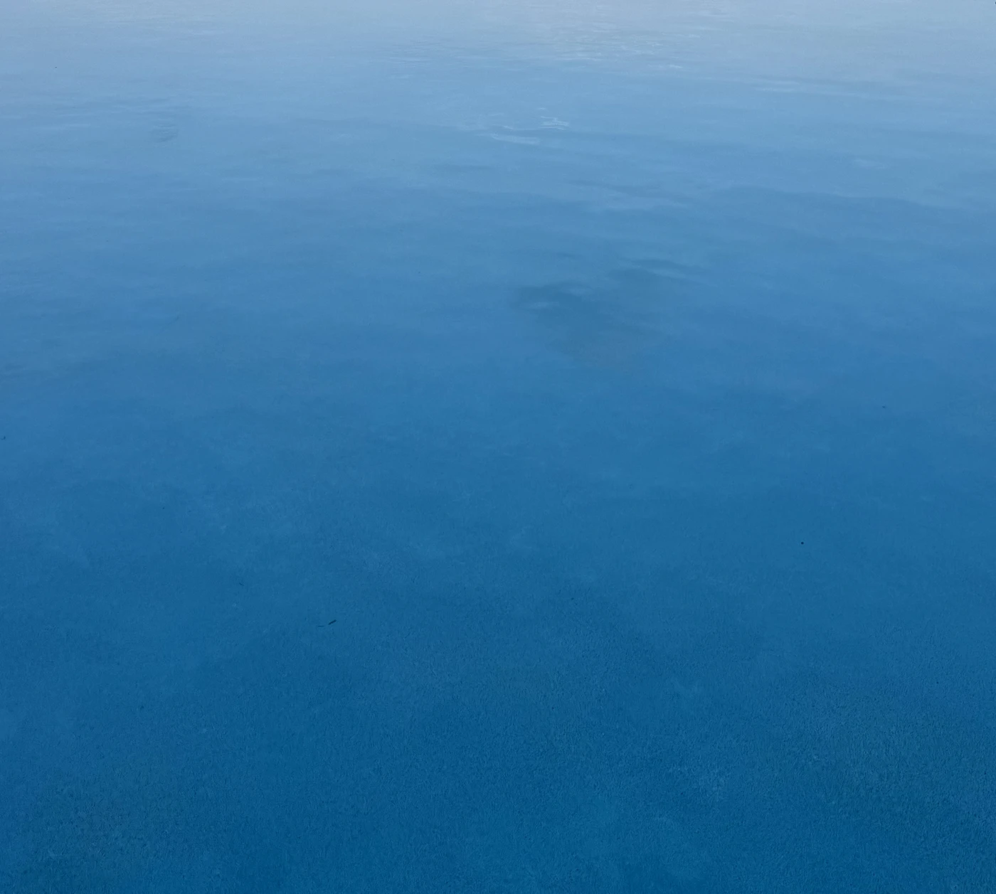 Calm blue water fading from pale surface to deep shadow