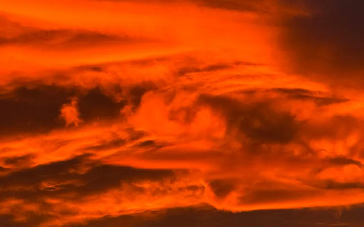 A sunset sky burning orange and red from edge to edge, layered clouds curling through the fire in bands of shadow.