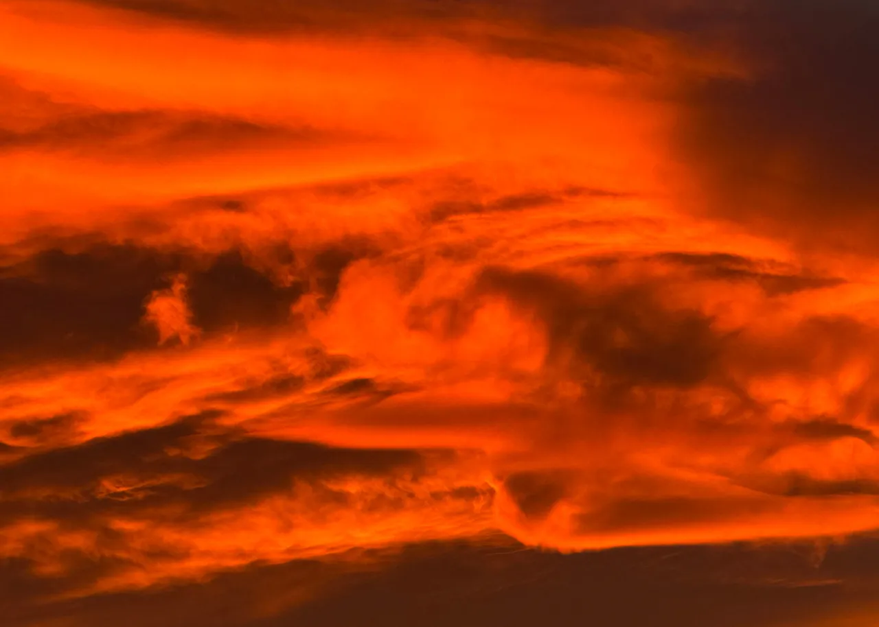 A sunset sky burning orange and red from edge to edge, layered clouds curling through the fire in bands of shadow.