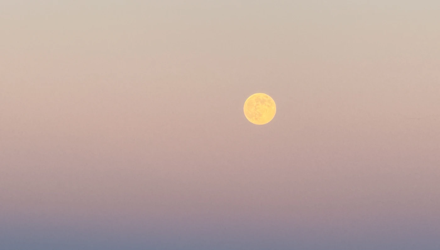 A pale full moon glowing in a soft gradient of pink and lavender dusk