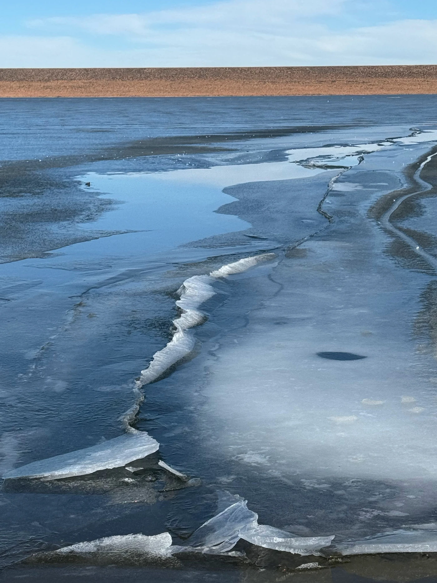 A jagged seam of ridged ice splitting the surface of a frozen blue lake